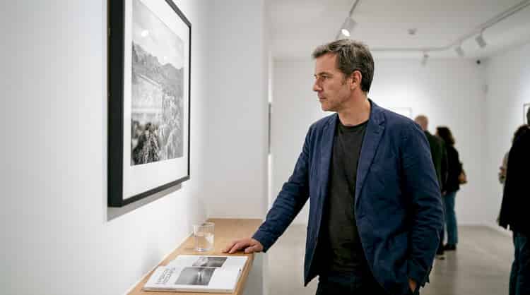 A man contemplates a portrait in an exhibition hall.